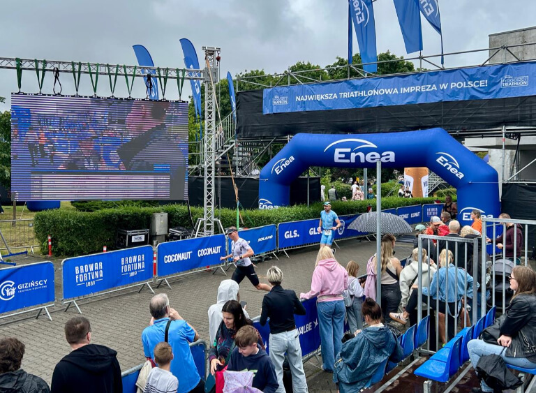 Strefa mety największej imprezy triathlonowej w Polsce z widocznym ekranem LED, balonem Enea oraz tłumem kibiców na trybunach i wzdłuż trasy