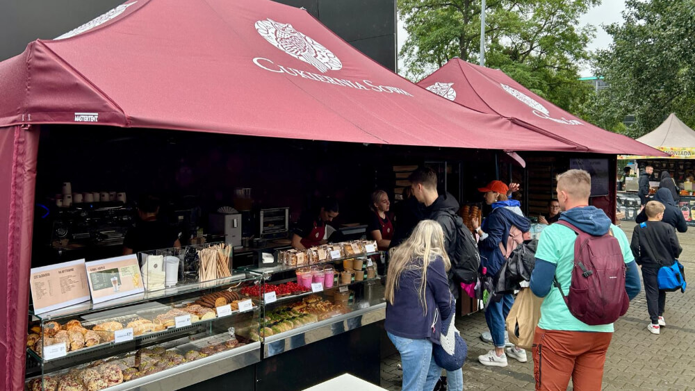 Stoiska Cukierni Sowa pod bordowymi namiotami z logo, z widoczną ladą pełną wypieków i klientów zamawiających desery oraz kawę